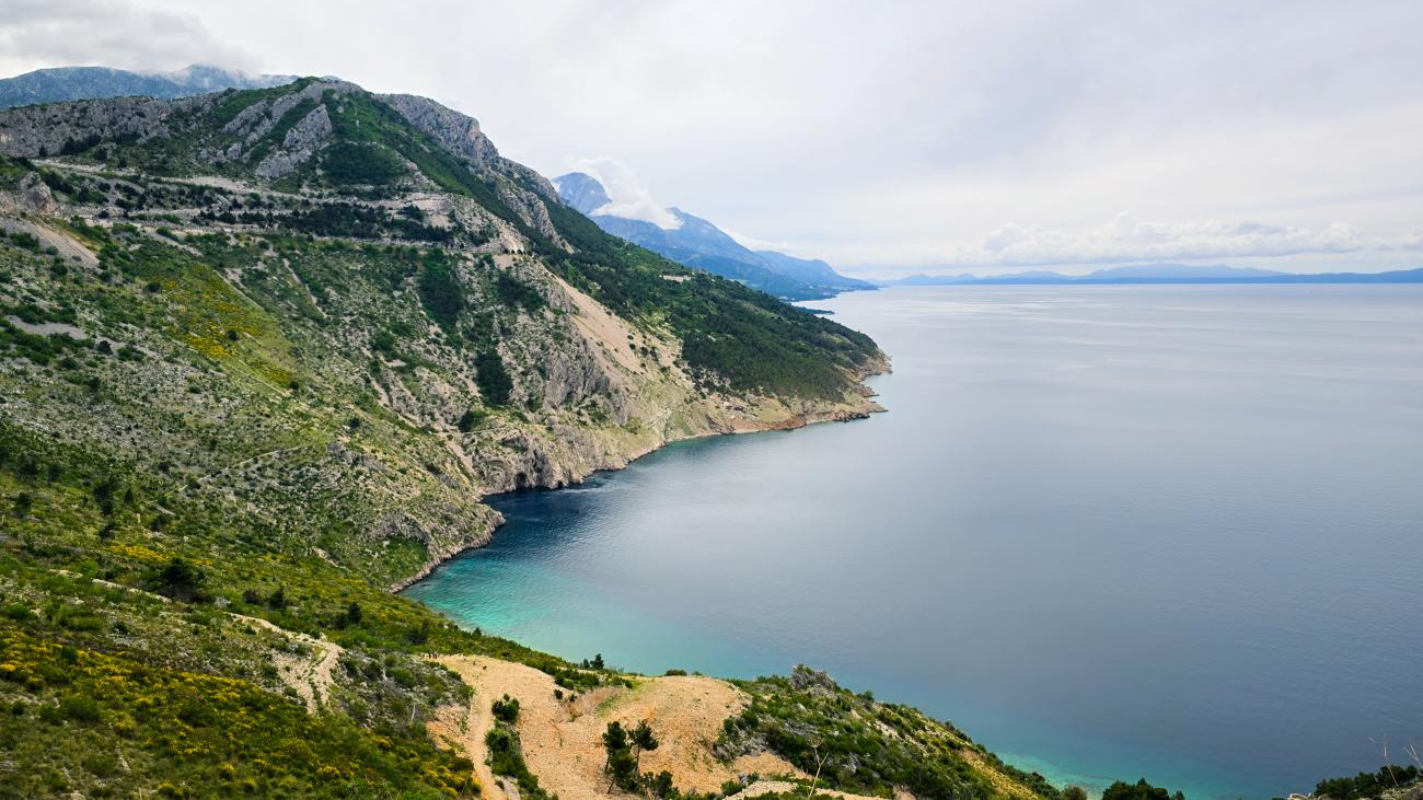 Dramatic view of the Croatian Adriatic coastline with steep green mountains meeting turquoise waters.