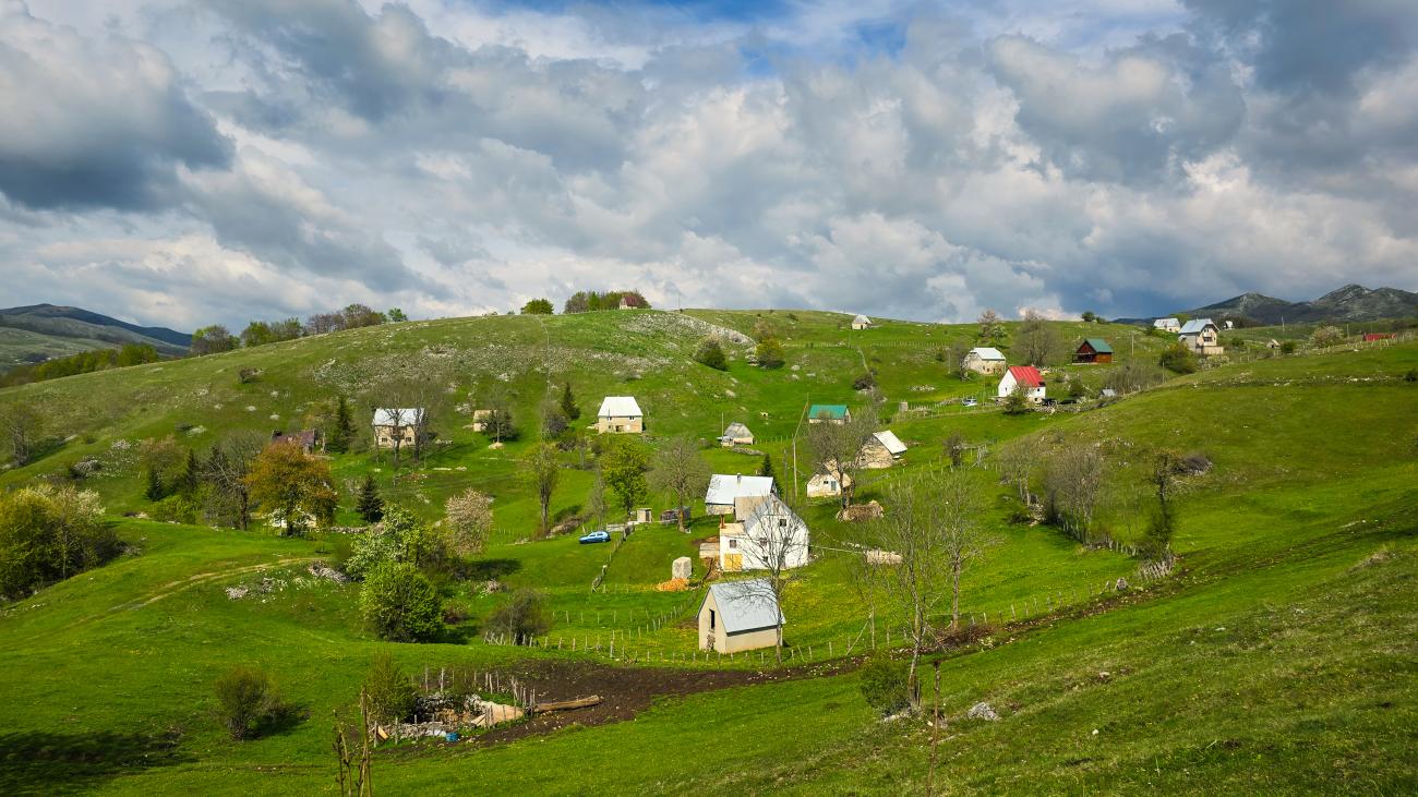 Scattered houses on a lush green hillside in the Bosnian countryside under dramatic clouds.