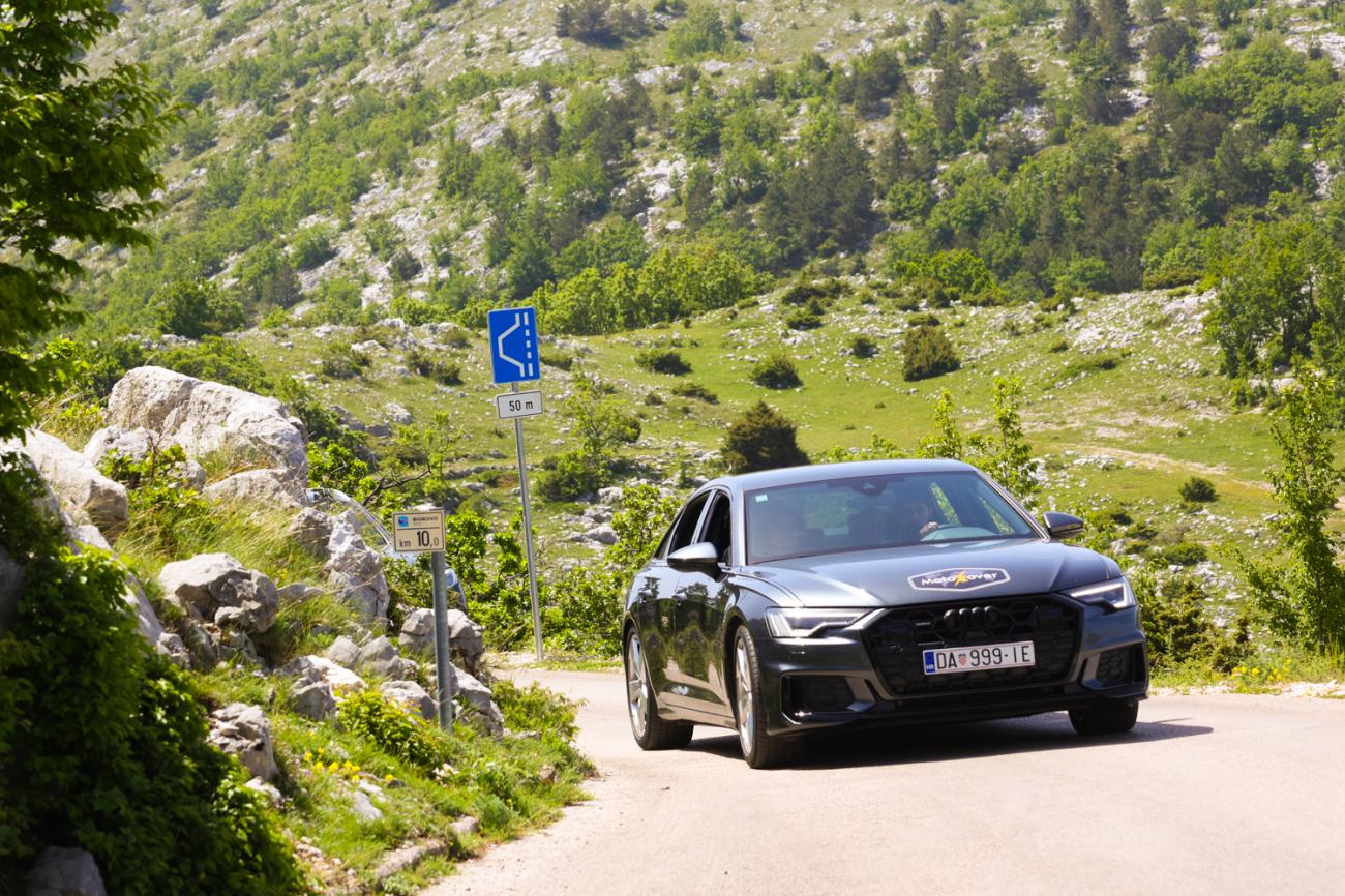 Audi sedan on a mountain road winding through rocky green hillside terrain in the Balkans