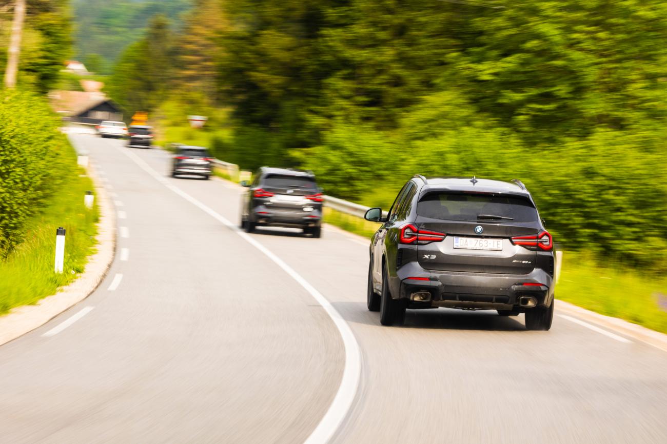 BMW X3 convoy navigating a winding road through dense green Balkan forest at speed