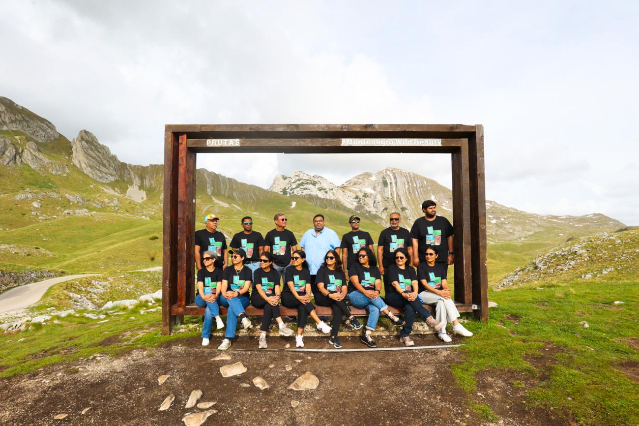 Tour group seated at a wooden frame viewpoint with the peaks of Durmitor National Park in Montenegro behind them