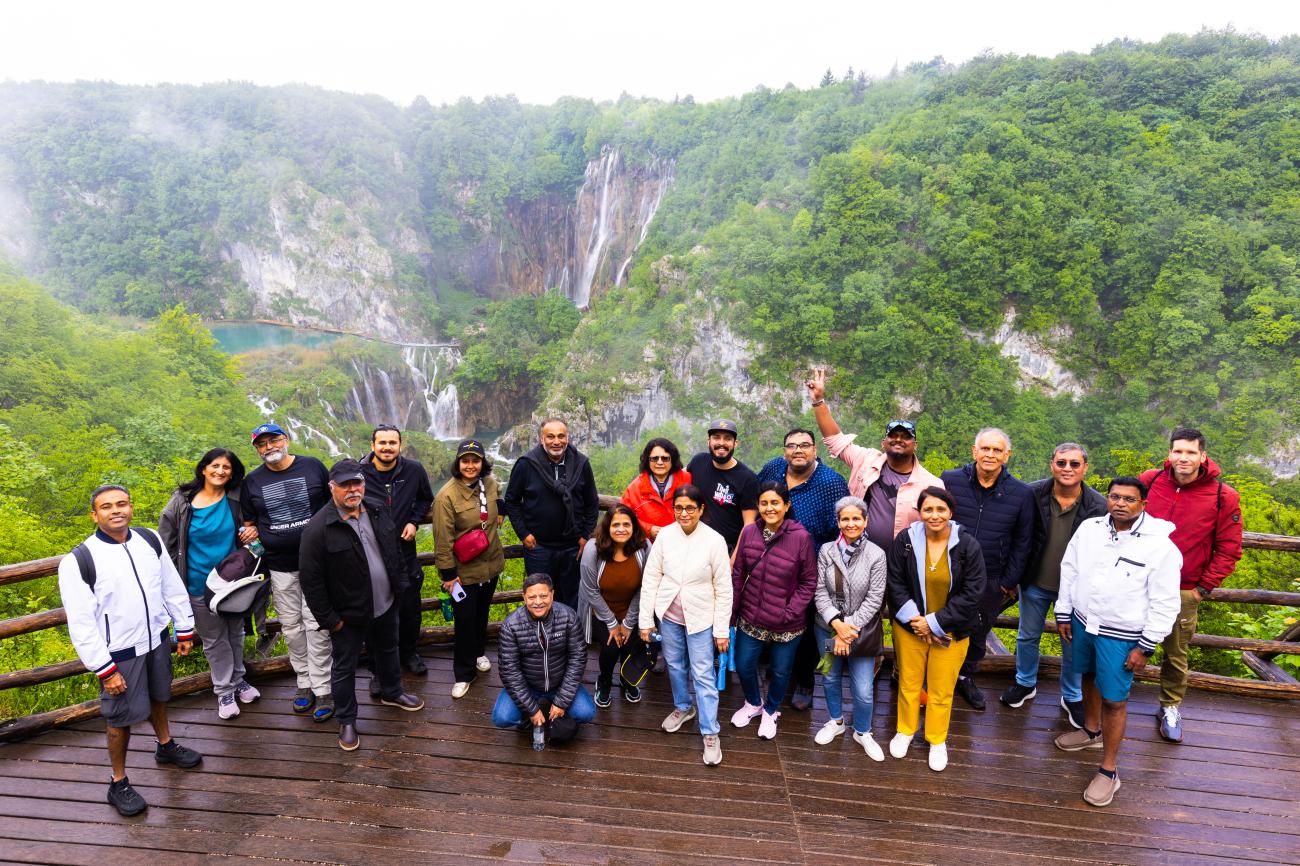 Tour group posing at a viewpoint overlooking waterfalls and turquoise lakes at Plitvice Lakes National Park in Croatia