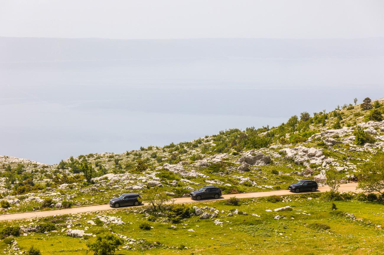 Three SUVs driving along a rugged coastal mountain road with the Adriatic Sea in the background