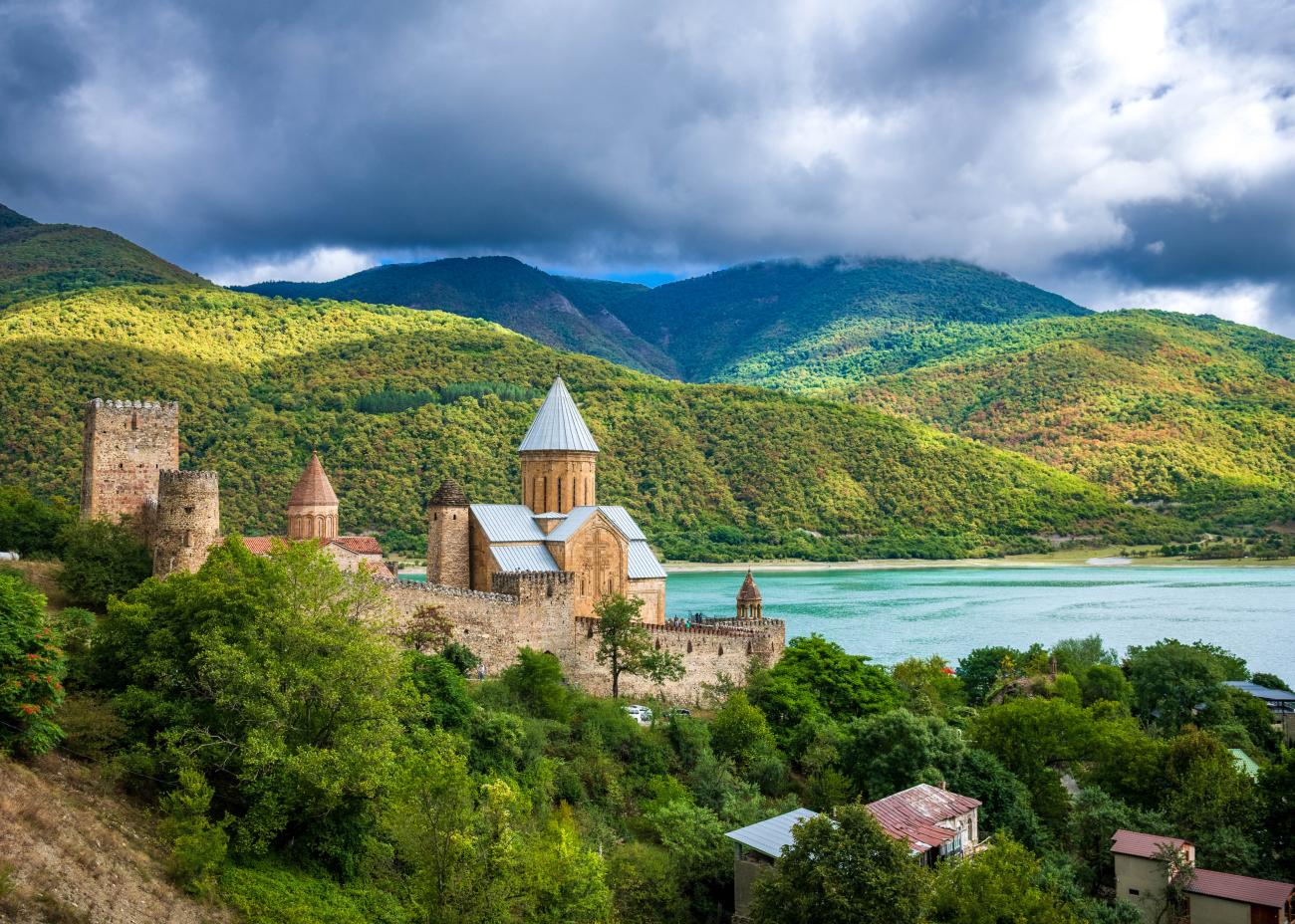 Ananuri fortress and church complex overlooking the turquoise Jinvali reservoir with green Caucasus hills.