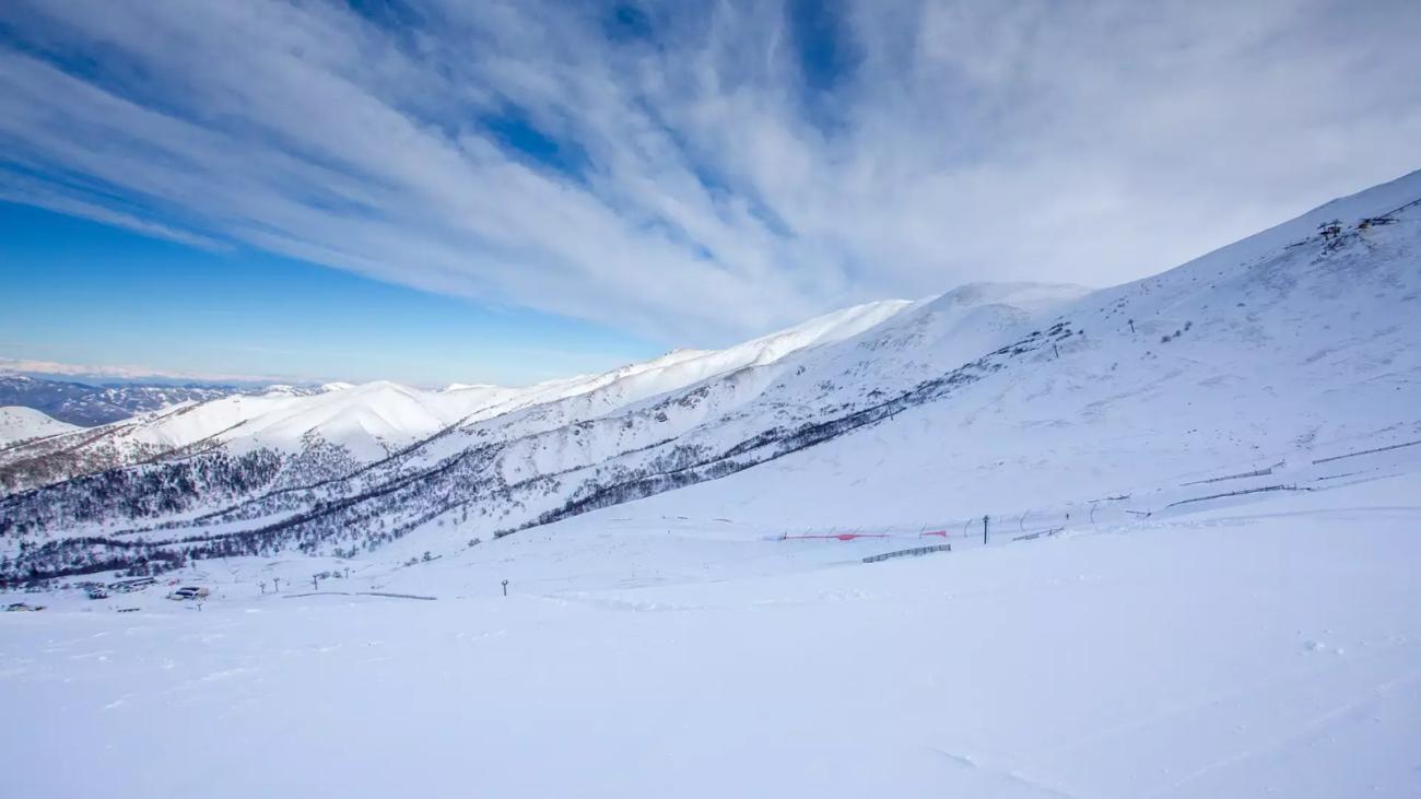A vast snow-covered ski resort landscape in the Georgian Caucasus under a bright blue sky with wispy clouds