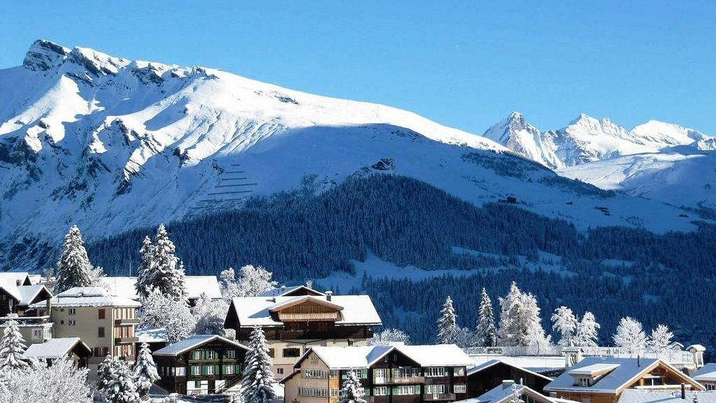 A picturesque snow-covered mountain village with traditional wooden chalets and snow-laden trees beneath the Caucasus peaks