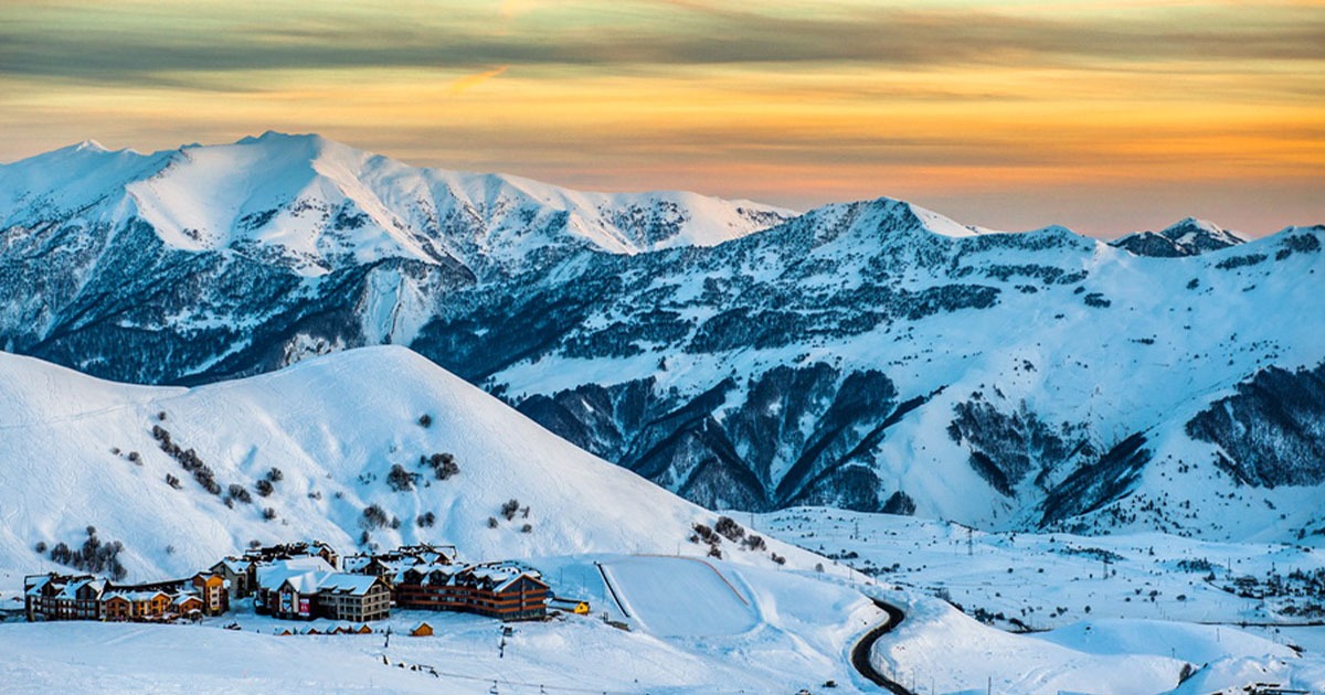 A stunning golden sunset over the snow-covered Caucasus mountains with the Gudauri ski resort village nestled in the valley below