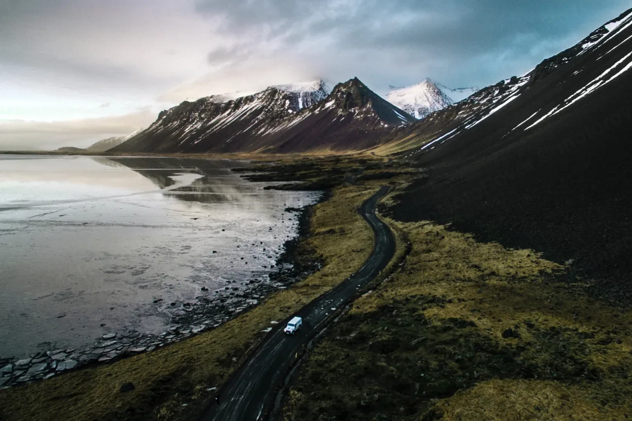 Aerial view of a road winding along an Icelandic fjord beneath snow-capped mountains