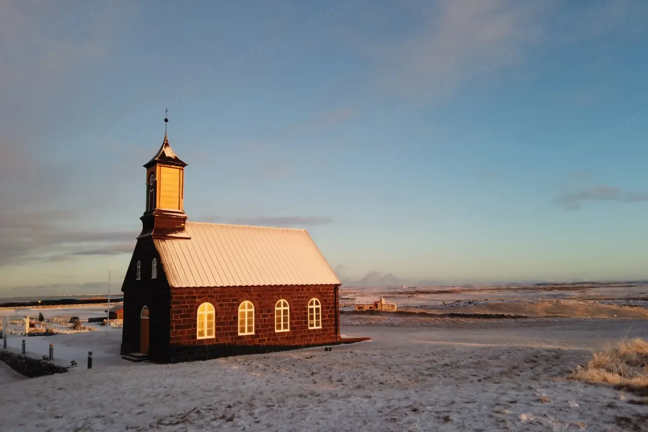 The stone Hvalsneskirkja church glowing in low evening light on the Icelandic coast