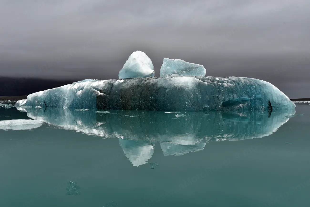 A blue iceberg reflected in the still water of the Jökulsárlón glacier lagoon