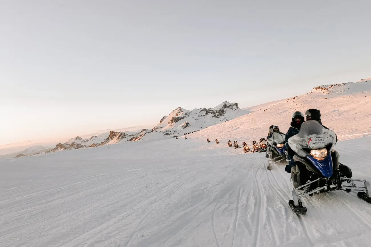A line of snowmobiles riding across a snow-covered Icelandic glacier