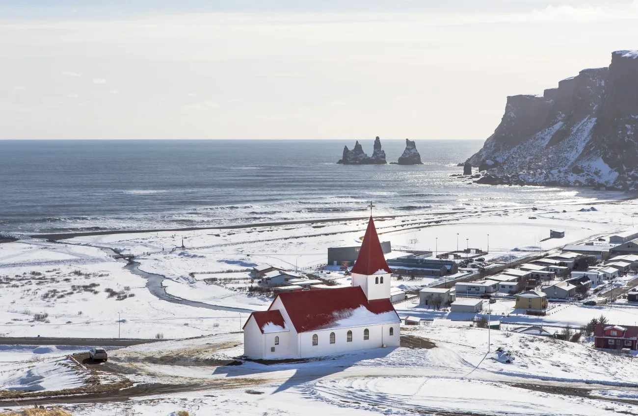 The red-roofed church above Vík with snowy fields and sea stacks on the south coast
