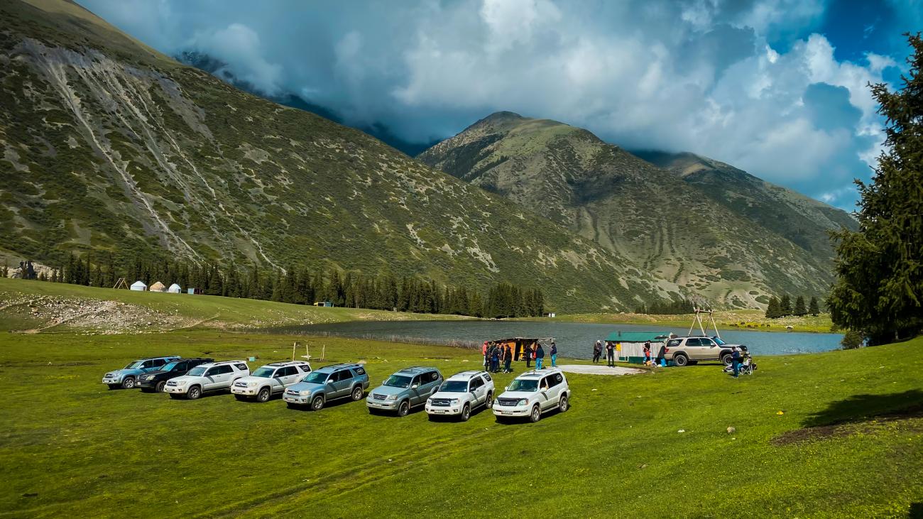 SUV convoy parked beside alpine lake on green meadow Kyrgyzstan