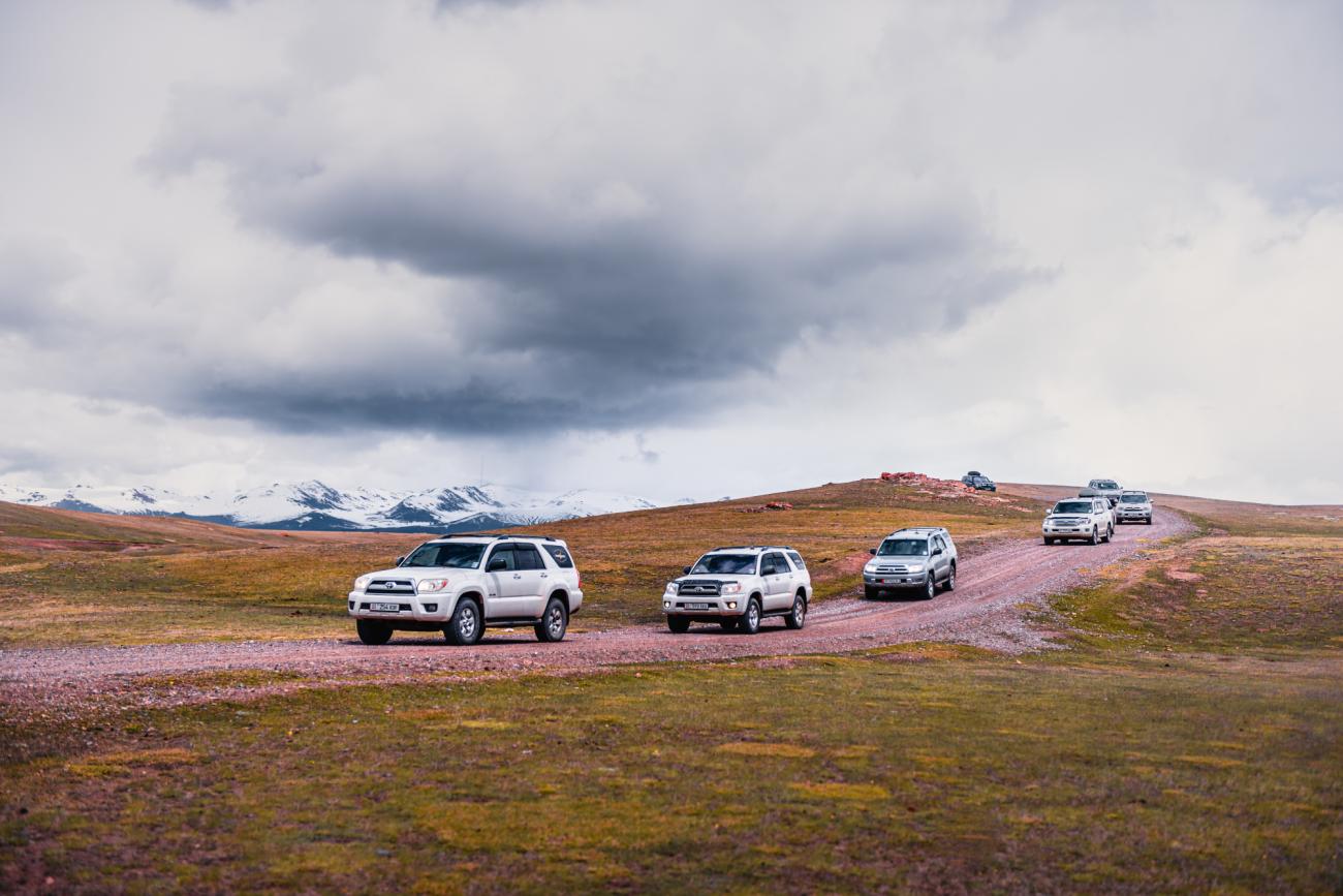 SUV convoy on highway with snowy mountains Kyrgyzstan