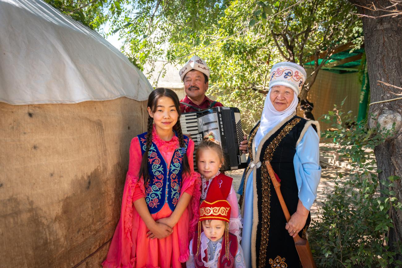 Kyrgyz family in traditional dress beside yurt with accordion