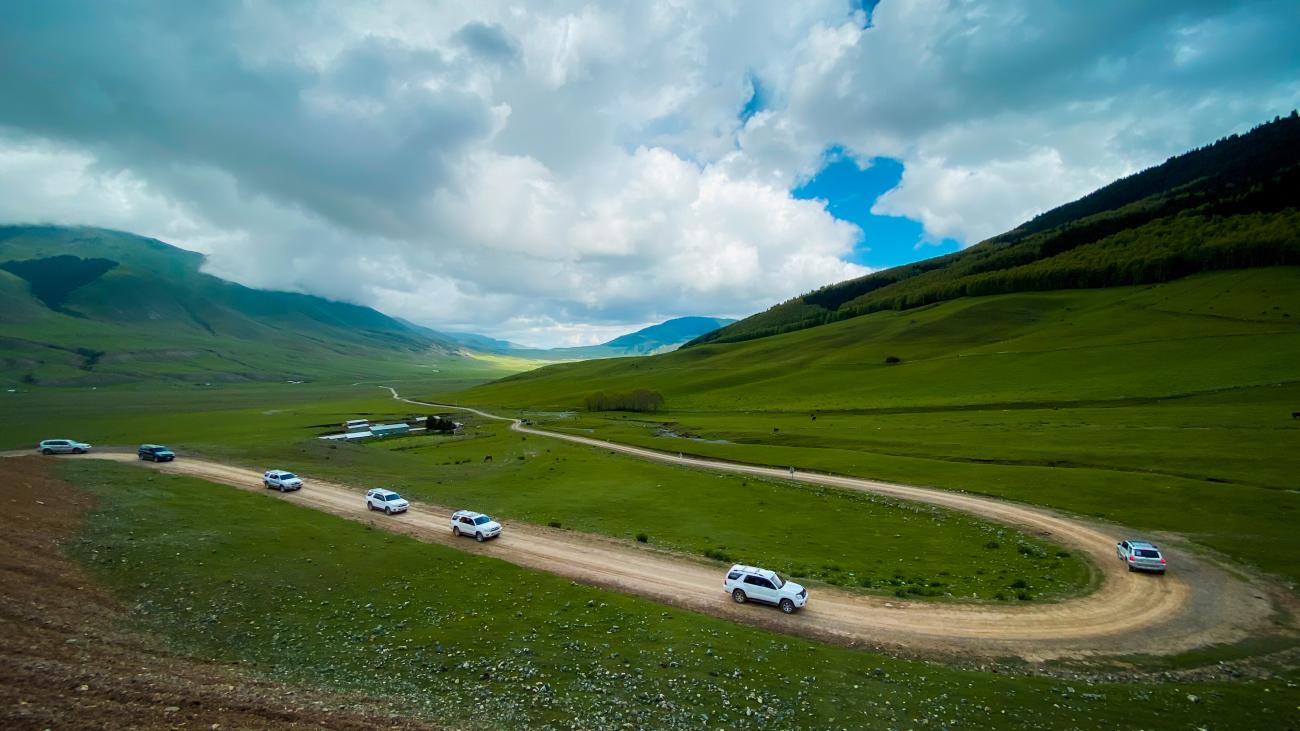 SUV convoy on mountain pass with dramatic clouds Kyrgyzstan