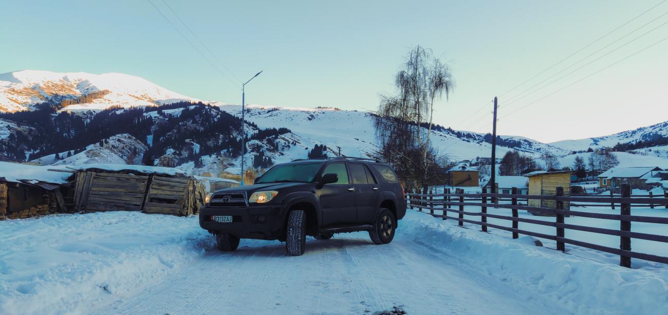 A 4x4 SUV parked on a snowy road in a Kyrgyz mountain village at golden hour