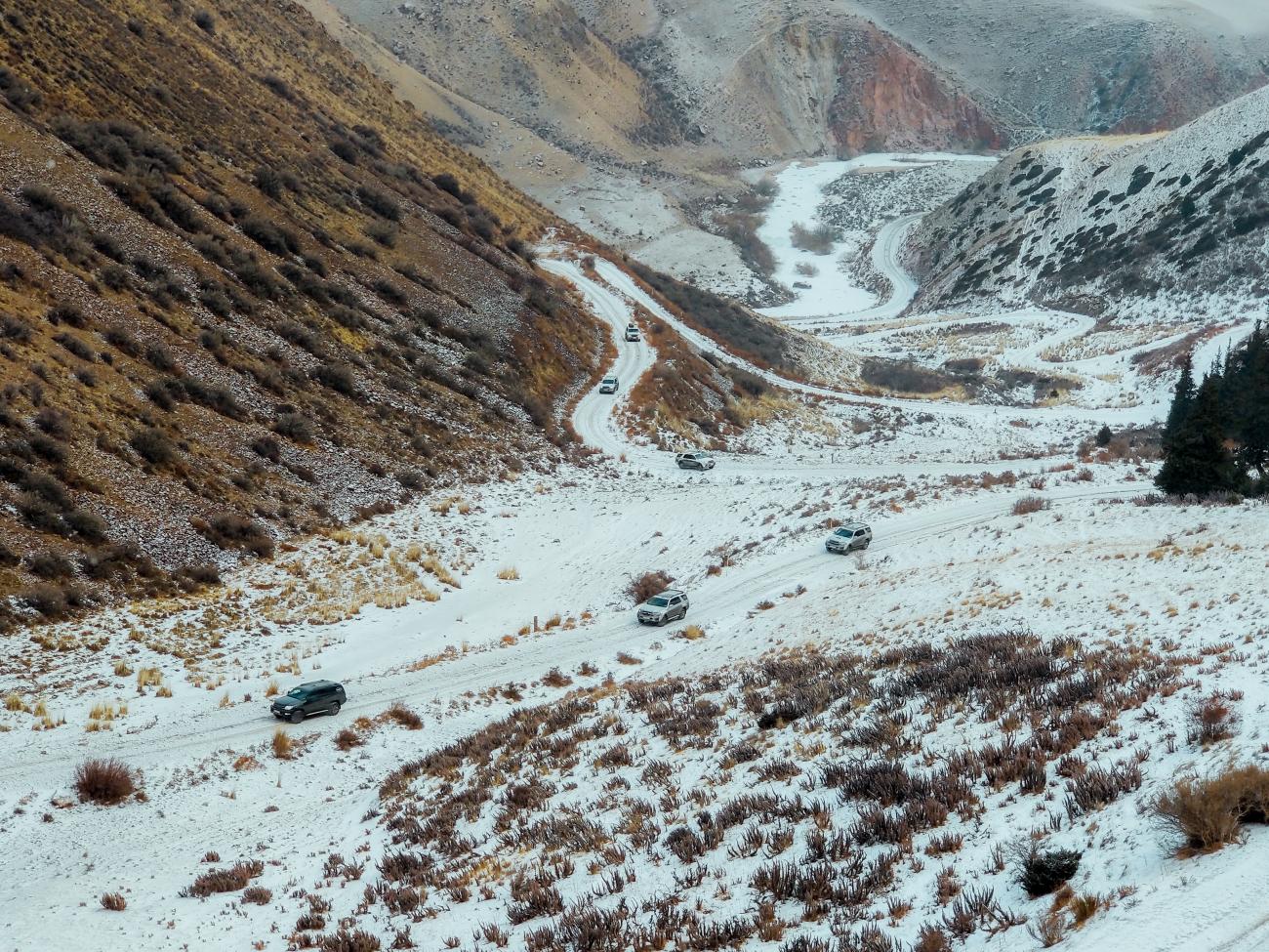 SUVs navigating a switchback road descending into a colorful mountain valley dusted with snow