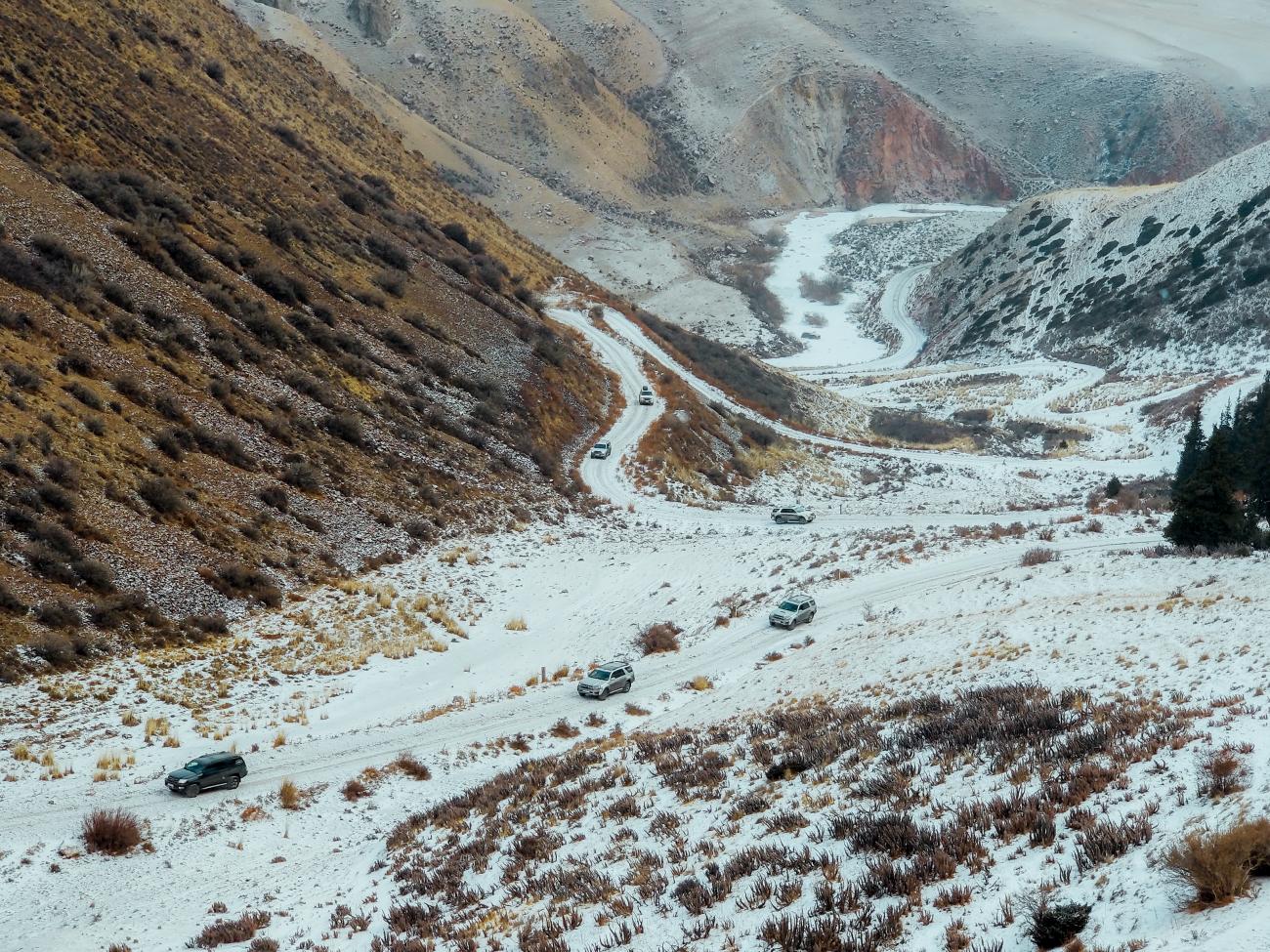4x4 vehicles descending a winding snowy road through a rugged canyon with red rock layers