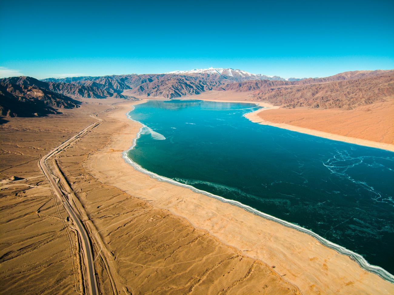 Aerial view of a turquoise alpine lake surrounded by arid desert mountains in Kyrgyzstan