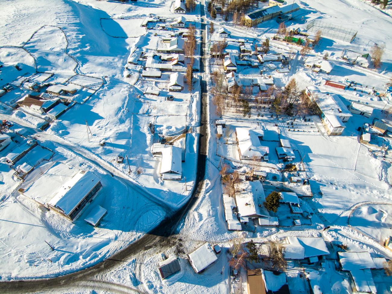 Drone view of a Kyrgyz village with snow-blanketed rooftops and a road cutting through the center