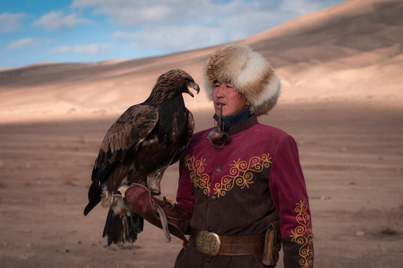 A young Kyrgyz eagle hunter in a purple embroidered coat with a golden eagle on his arm