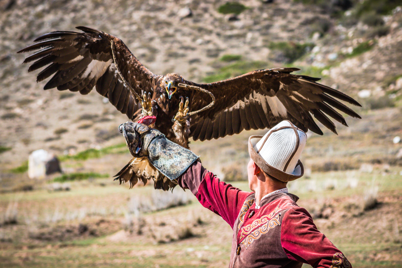 A Kyrgyz eagle hunter in traditional dress with a golden eagle perched on his arm