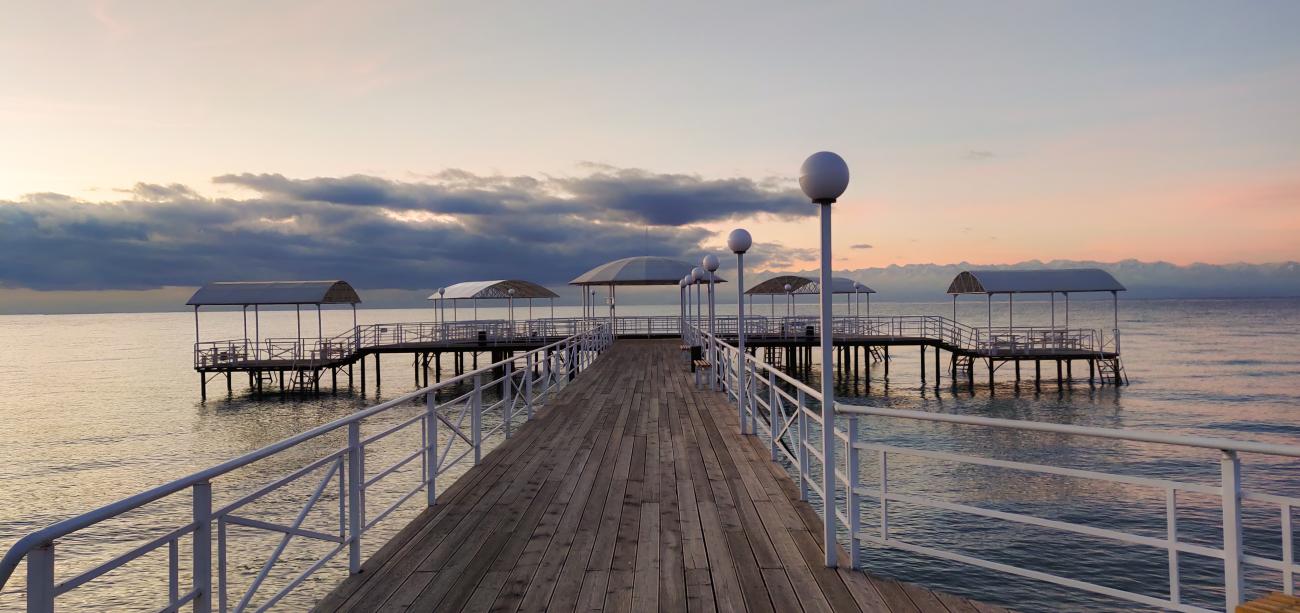 A wooden pier extending over the calm waters of Issyk-Kul lake at sunset with dramatic clouds