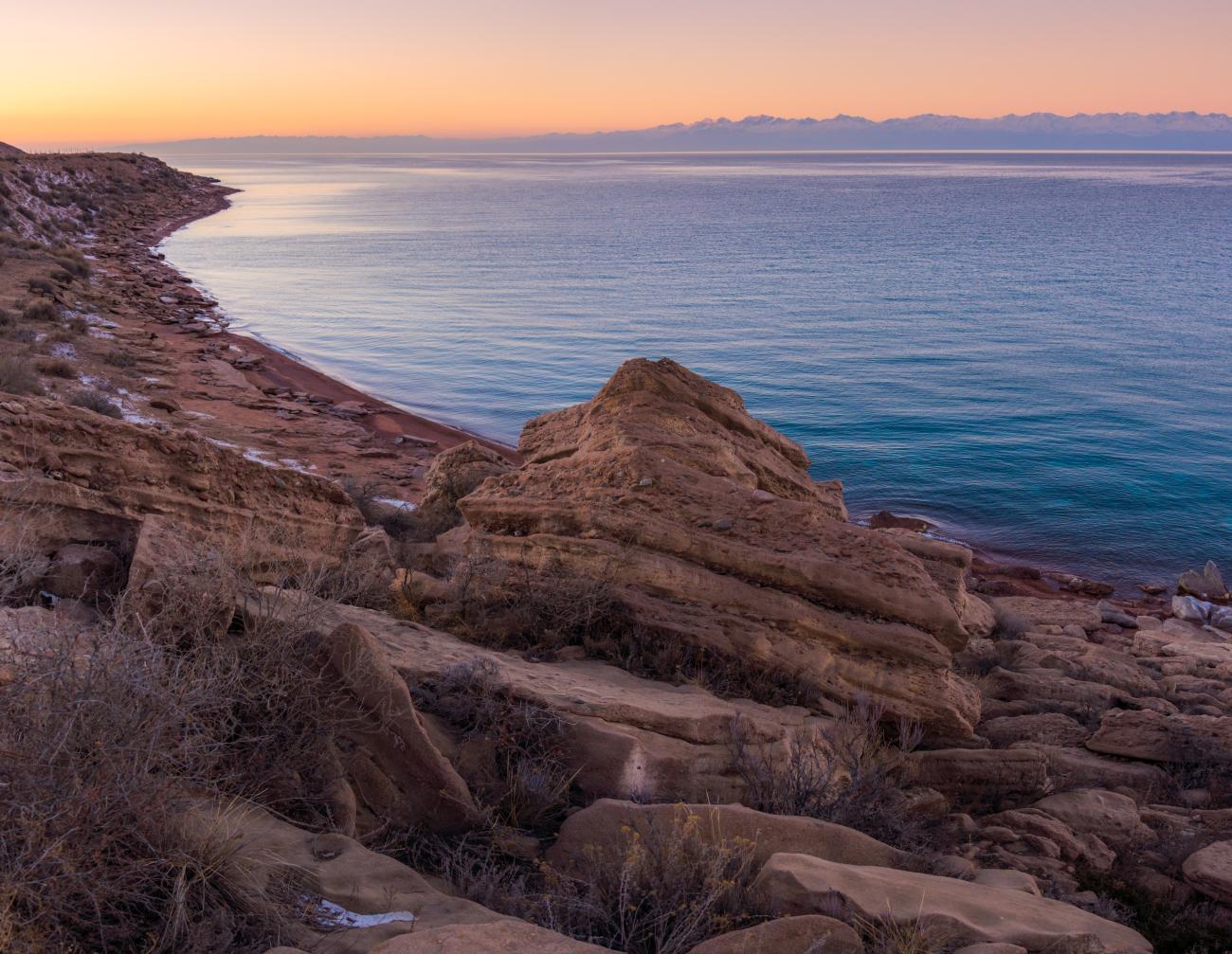 Rocky shoreline of Issyk-Kul lake at sunset with warm golden light over the calm water