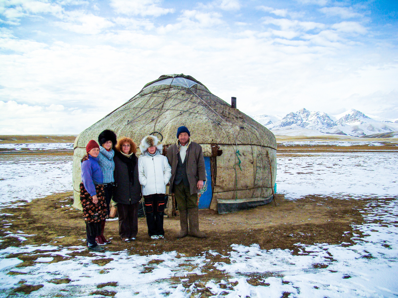 A Kyrgyz nomad family posing in front of their traditional yurt with snow-capped mountains in the distance
