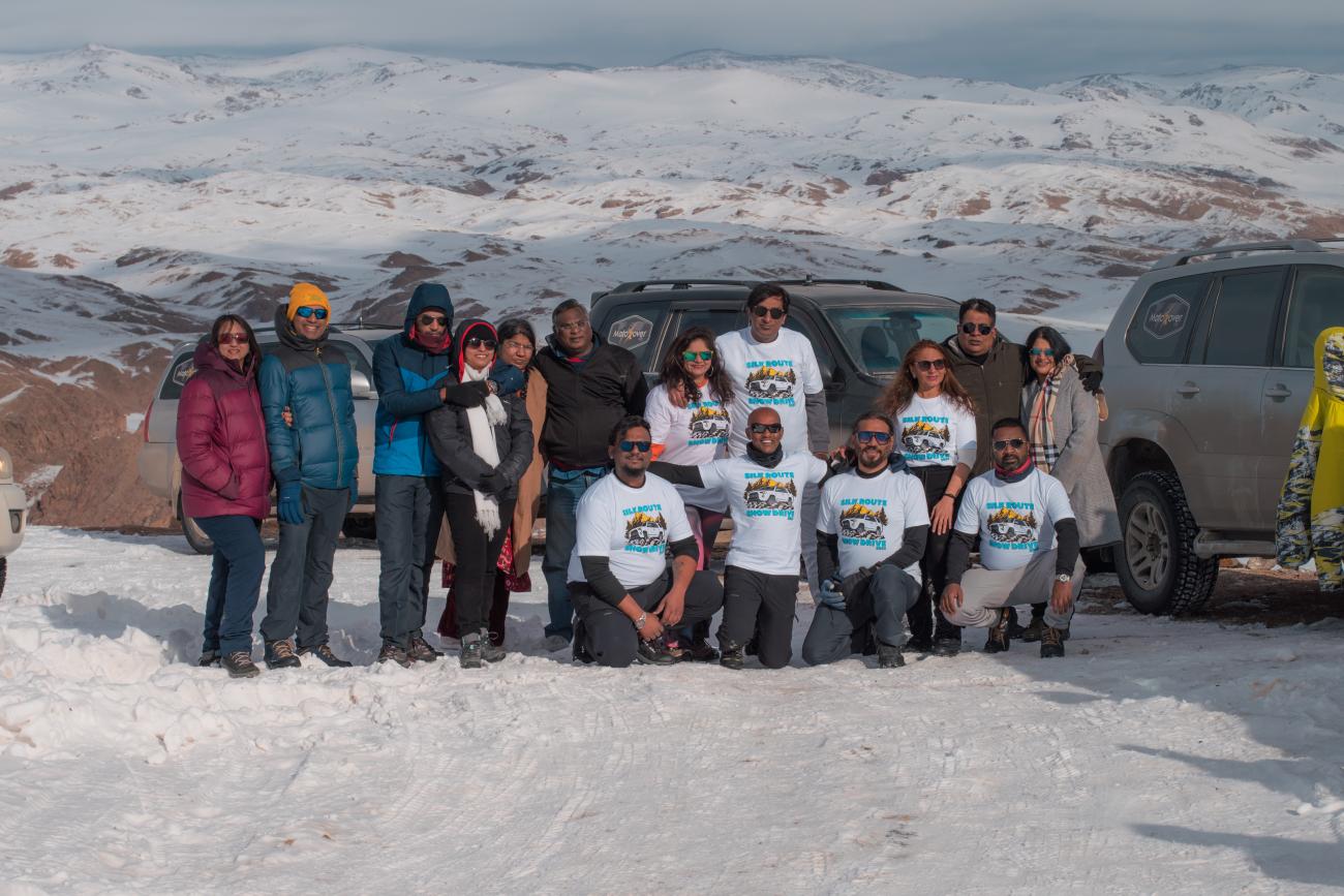 The Kyrgyzstan Snow Drive tour group posing with their 4x4 vehicles on a snowy mountain pass