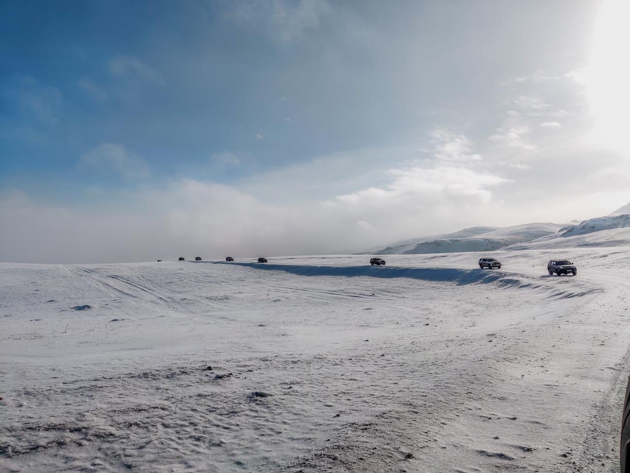 Multiple 4x4 vehicles spread across a vast snow-covered steppe under a cloudy winter sky