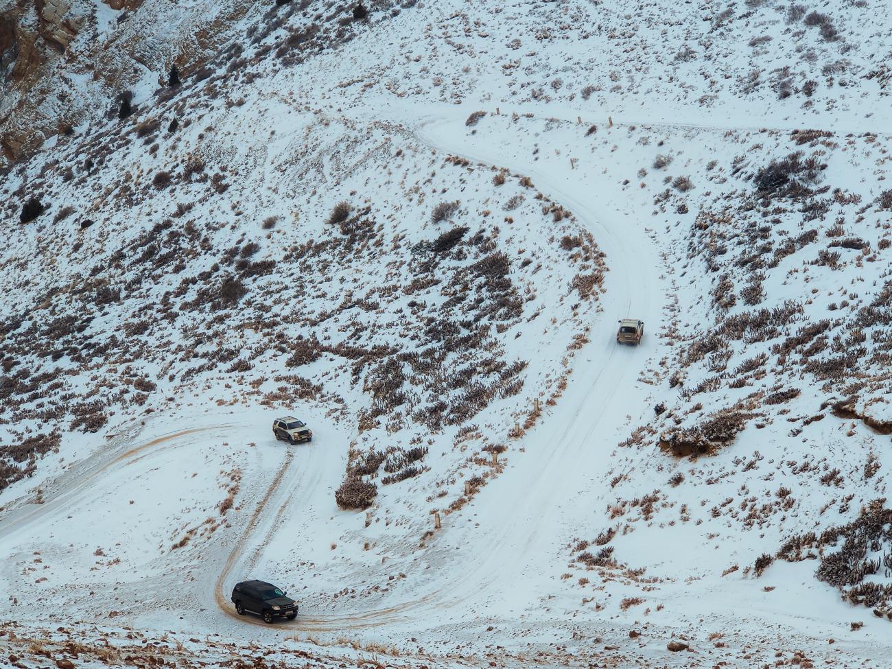 Three SUVs climbing a series of switchbacks on a snow-dusted mountain hillside