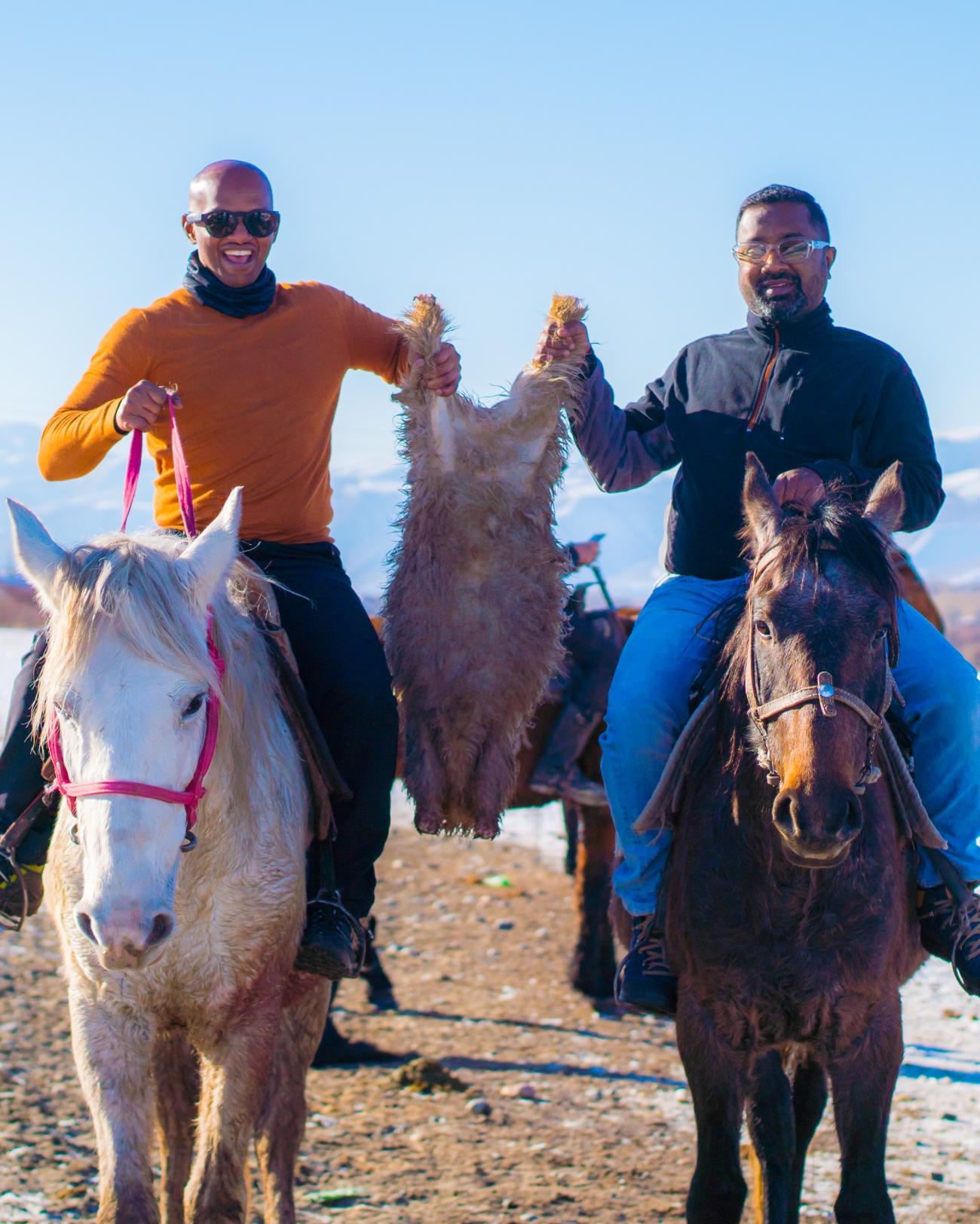 Two travelers on horseback holding a goat skin during a traditional kok-boru game in Kyrgyzstan