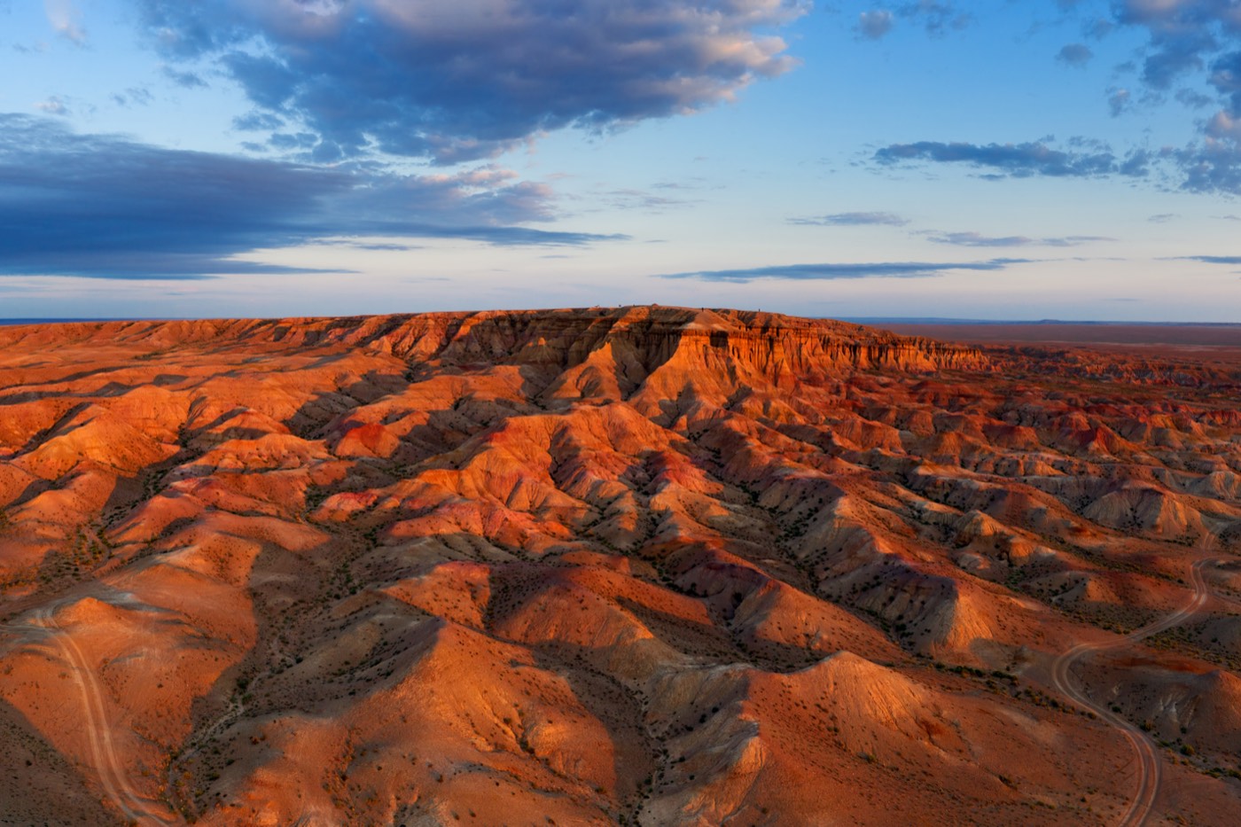 Aerial view of the layered orange badlands of Tsagaan Suvarga canyon lit by the setting sun
