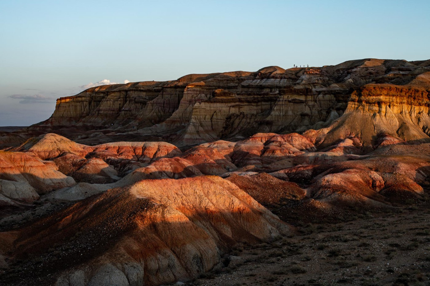 Visitors standing atop the sunset-lit badland cliffs of Tsagaan Suvarga, the "White Stupa"