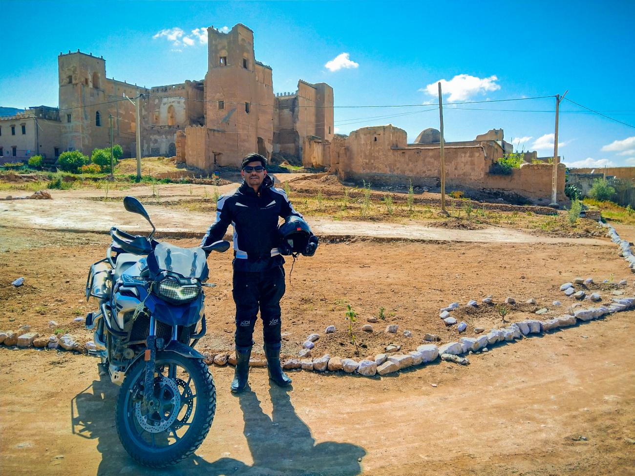 A rider standing with his motorcycle in front of ancient kasbah ruins in Morocco.