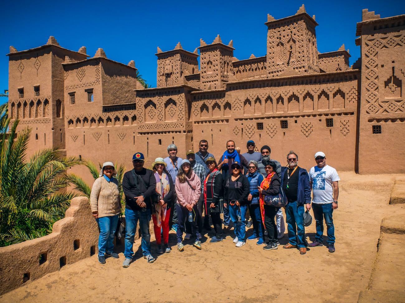 Tour group posing in front of the ornate mud-brick towers of Kasbah Amridil in Skoura, Morocco.