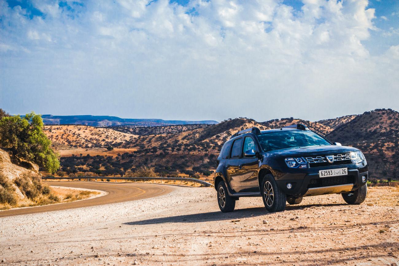 Black Dacia Duster on a winding hillside road through the arid Moroccan countryside.