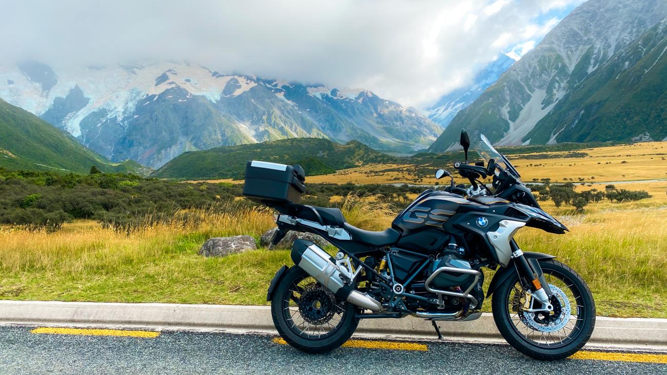 BMW R1250GS parked roadside with a sweeping view of Mount Cook glaciers and golden tussock grasslands.