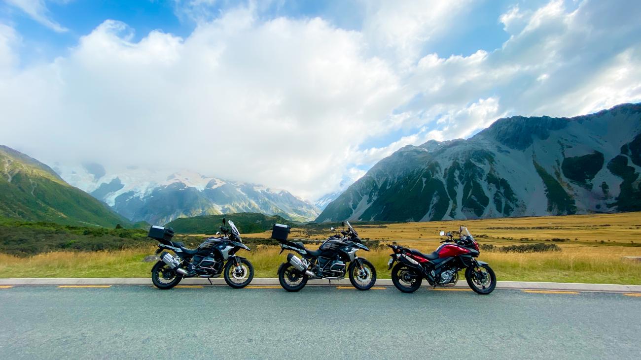 Three touring motorcycles parked on a road with glaciers and the Mount Cook valley stretching out behind them.