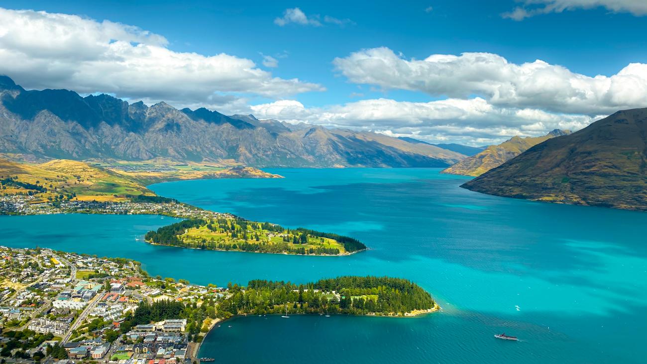 Aerial view of Queenstown on the shores of turquoise Lake Wakatipu with the Remarkables mountain range in the background.