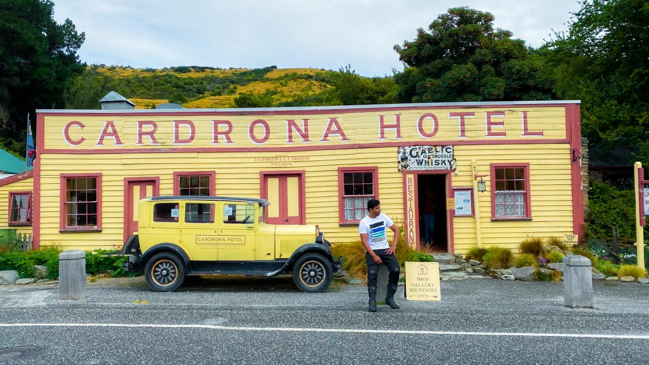 Historic yellow Cardrona Hotel with a vintage car parked outside, a classic landmark on the Crown Range route in New Zealand.