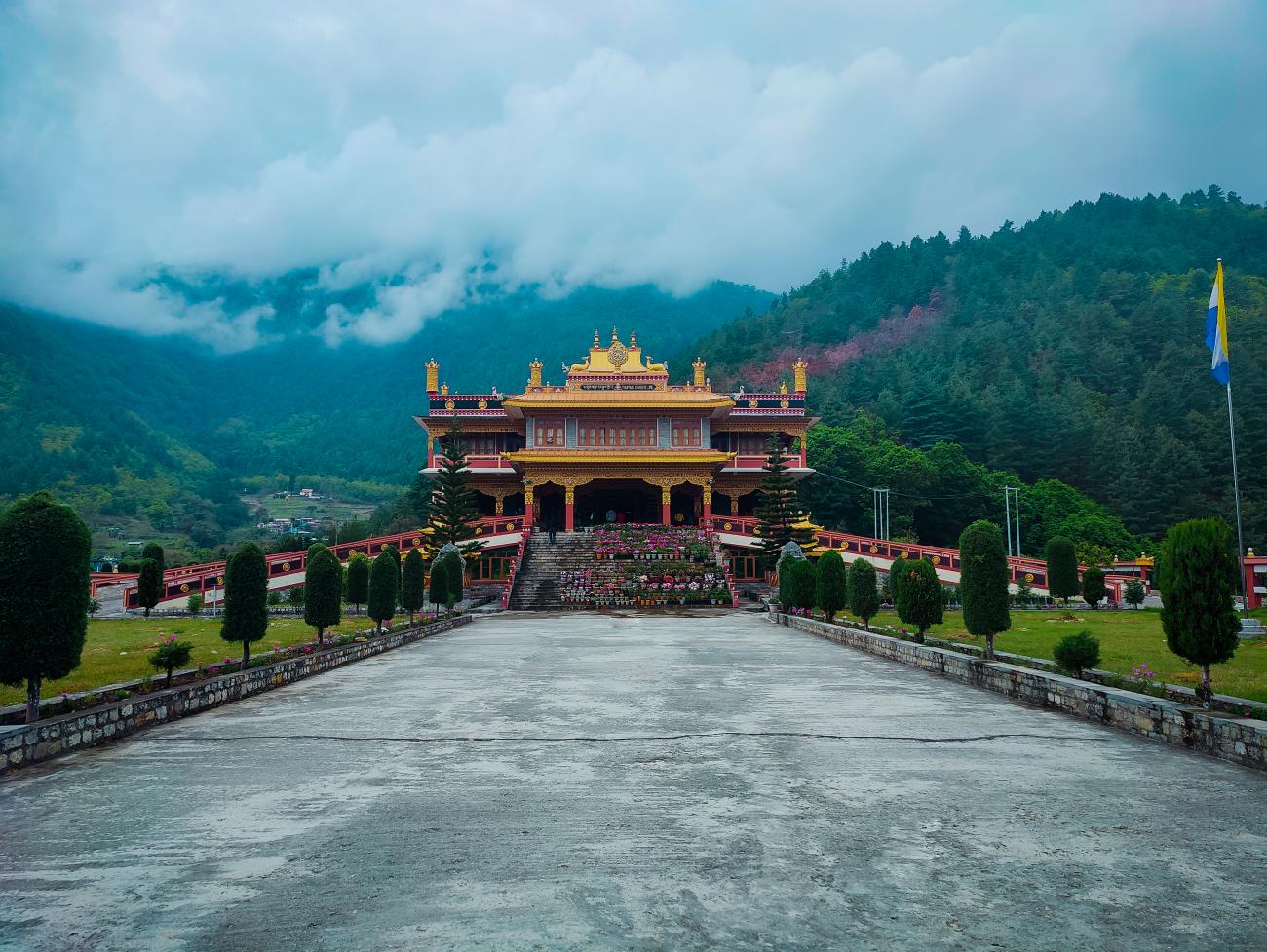 A grand golden Buddhist monastery set against cloud-draped forested mountains in Arunachal Pradesh.