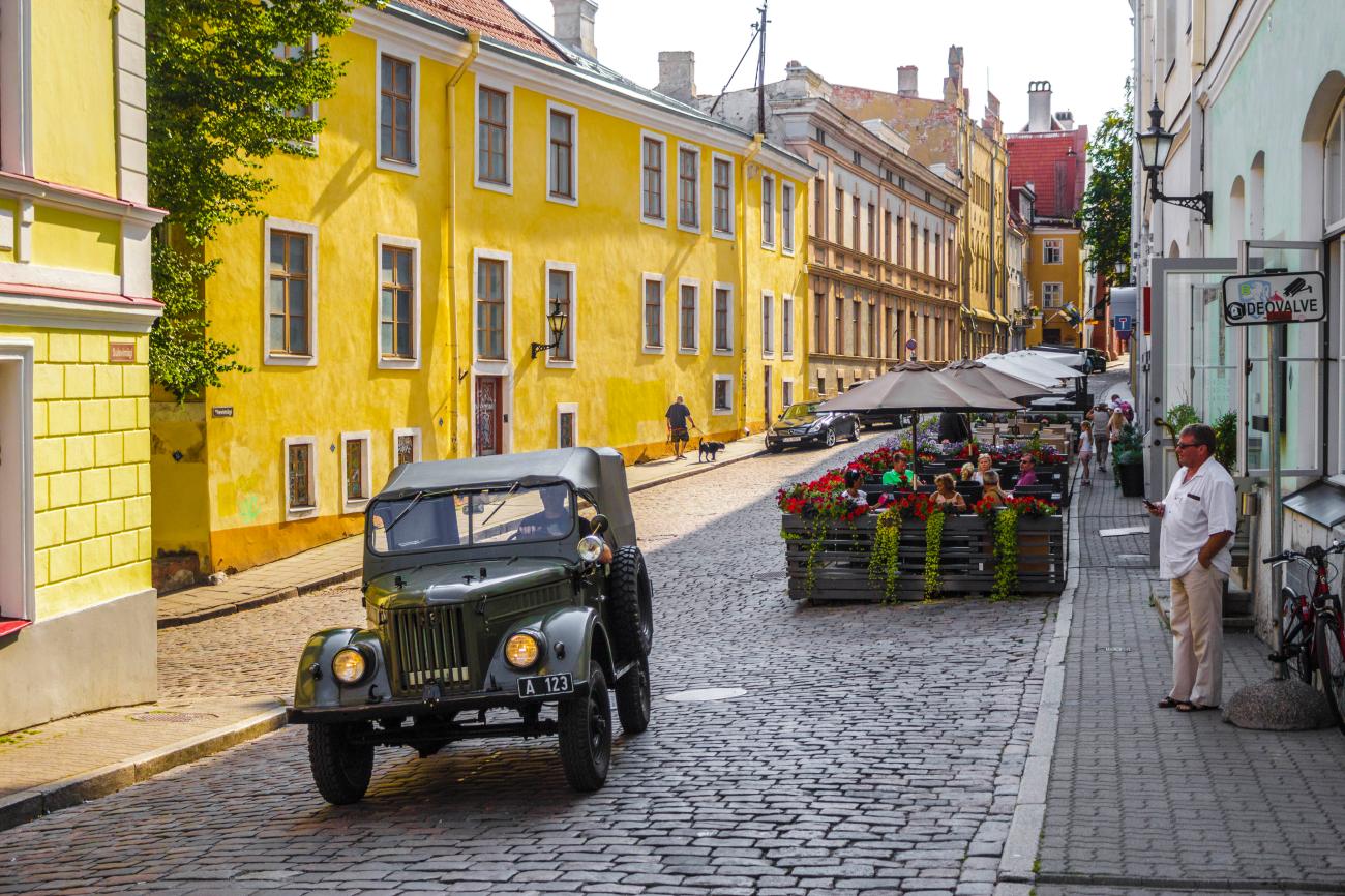 Cobblestone street with colorful buildings and a vintage military vehicle in Tallinn Old Town, Estonia.
