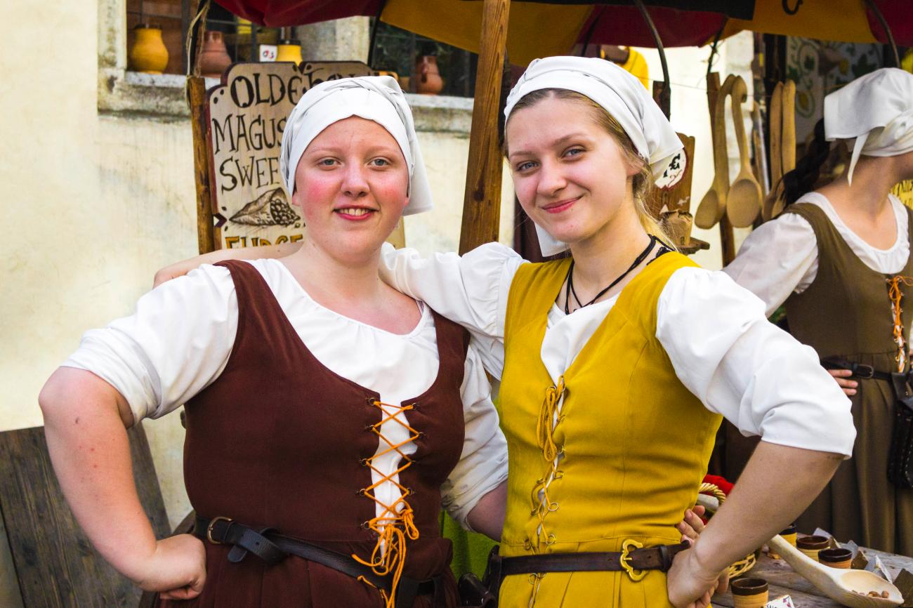 Two women in traditional medieval costumes at an old town market stall in the Baltics.
