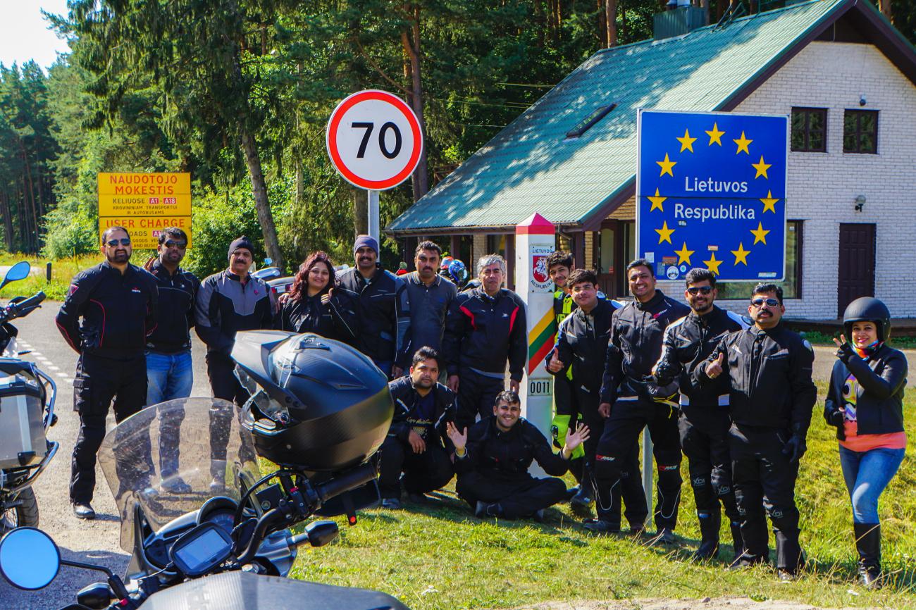 Motorcycle tour group posing at the Lithuania border sign during a Northern Europe ride.