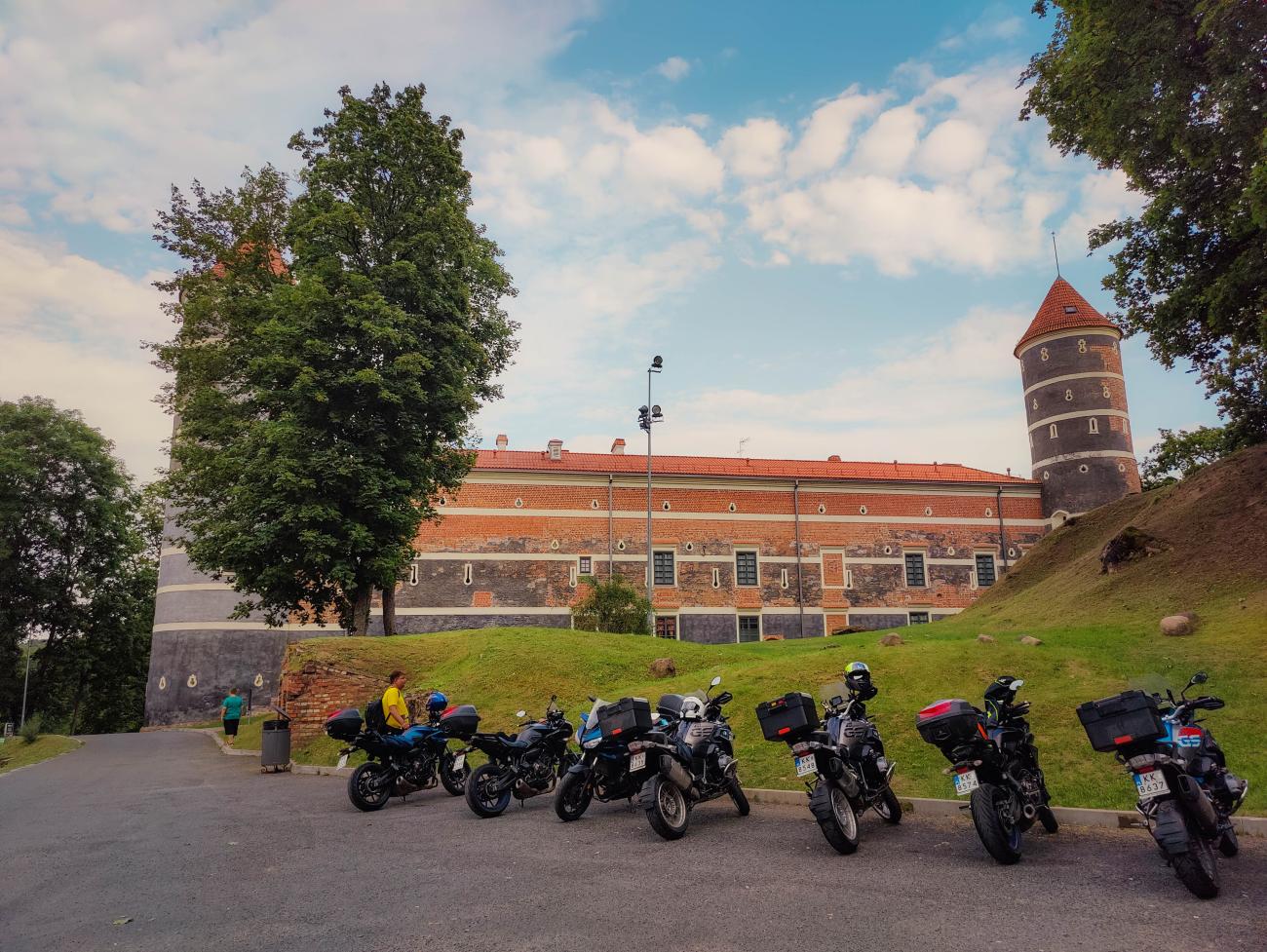 Adventure motorcycles parked in front of a medieval brick castle with a tower in Lithuania.
