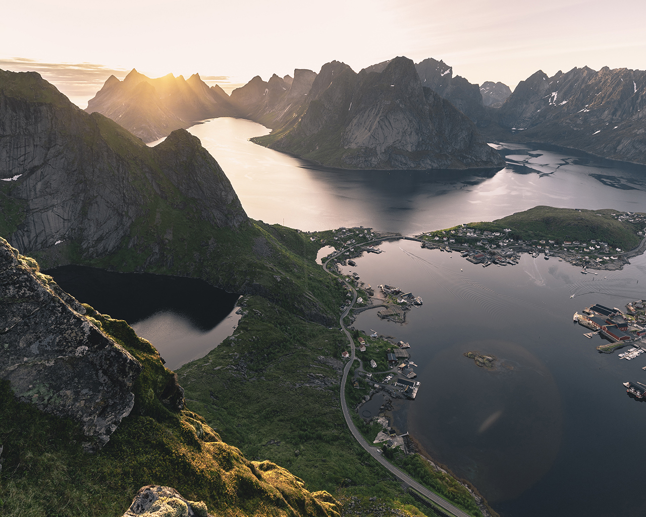 Sunset over Reine in the Lofoten Islands with jagged peaks, fjords, and a village seen from a mountain summit.