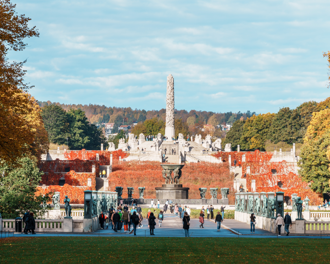 Visitors strolling through Vigeland Sculpture Park in Oslo with the Monolith column and autumn foliage.